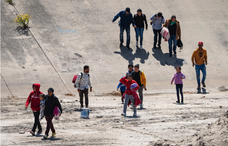 People cross the Tijuana River and move toward the US border wall in Tijuana, Mexico, on May 11, 2023. John Fredricks/The Epoch Times